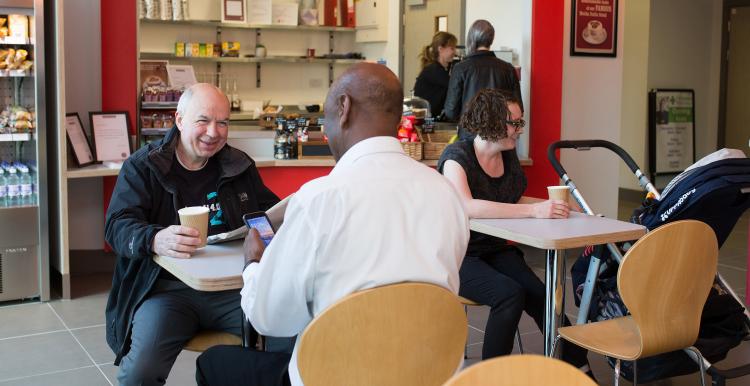 Two males sat in a coffee shop, talking and laughing 